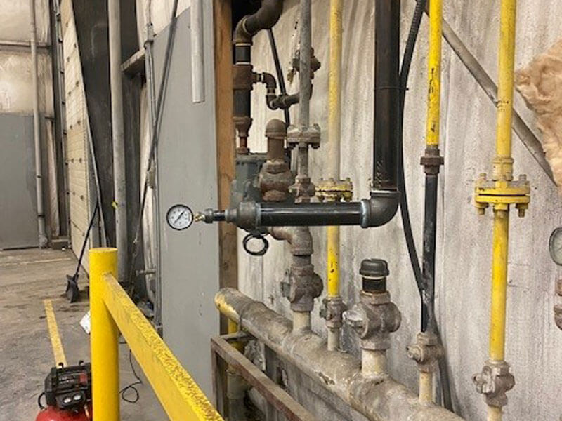 Industrial gas line with multiple valves and a pressure gauge inside a facility in Edmonton, AB.