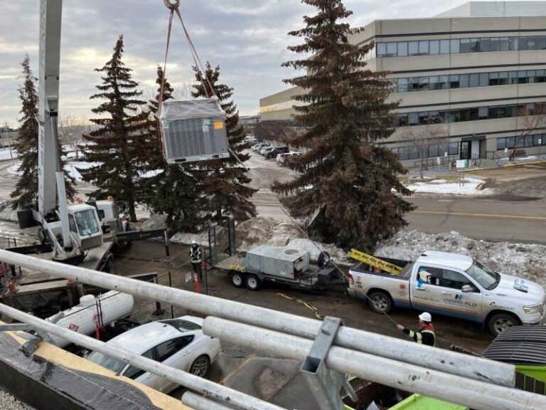 A crane lifts large equipment at a commercial HVAC installation site in Edmonton, AB