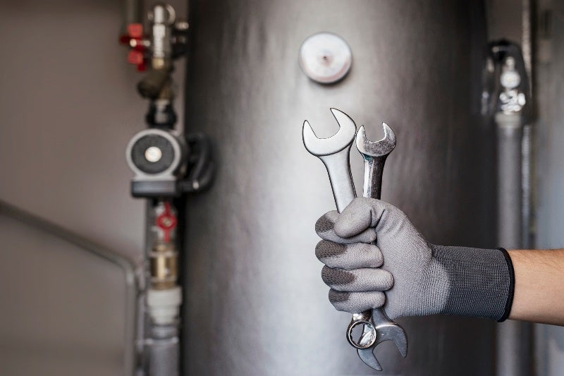 A hand holding wrenches in front of a water heater by Hydro-Flo Plumbing & Heating