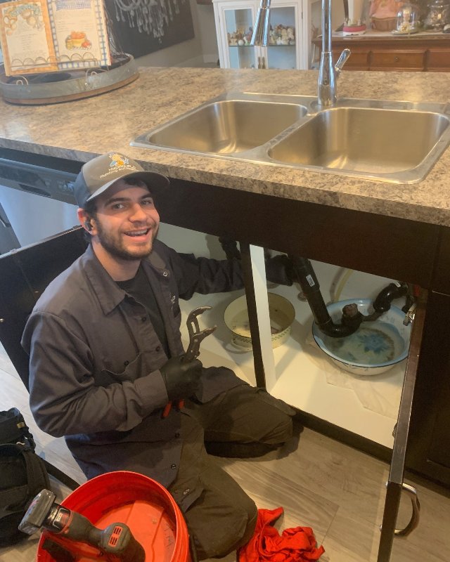 A plumber from Hydro-Flo Plumbing & Heating smiling while working on a kitchen sink