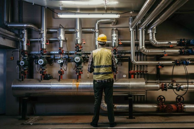 Commercial plumber in yellow hard hat inspecting industrial pipes