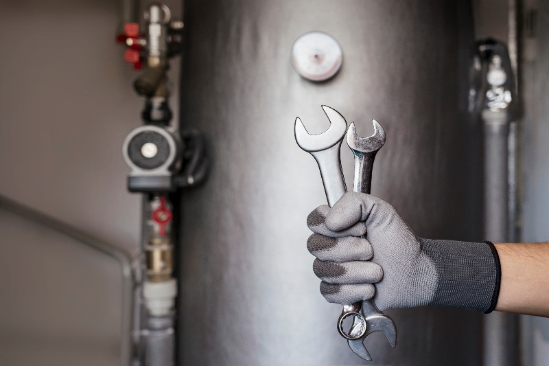 A hand holding wrenches in front of a water heater by Hydro-Flo Plumbing & Heating